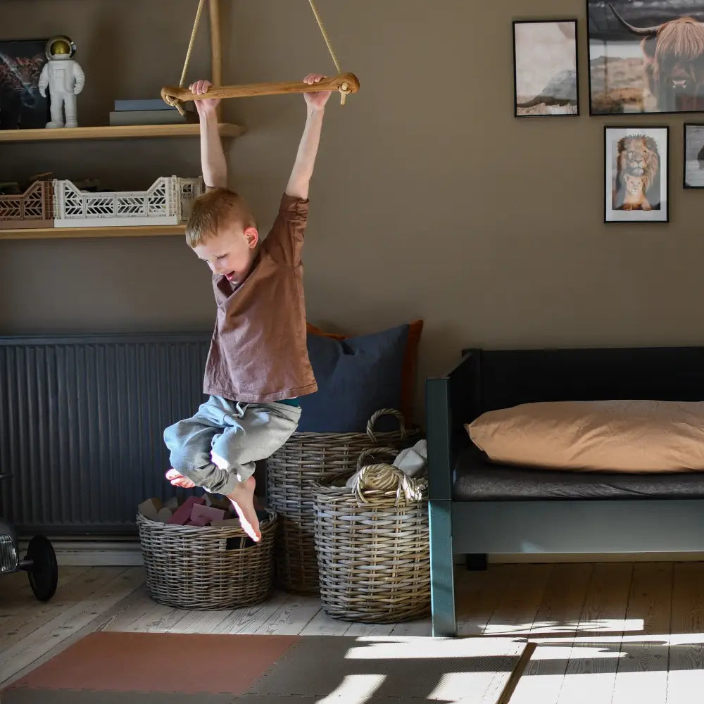 A child hangs from a bone oak green wooden monkey bar with rope suspension in a cozy neutrally toned room