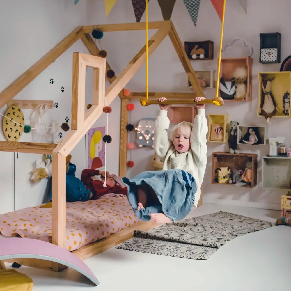 A child hangs from a wooden swing with yellow ropes inside a cozy oak green bone playhouse bed frame