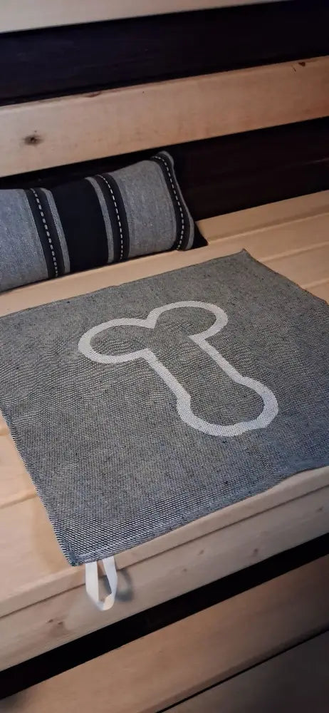 Gray woven sauna mat pefletti kalunalunen with white embroidered bone design and two white fabric ties at the bottom