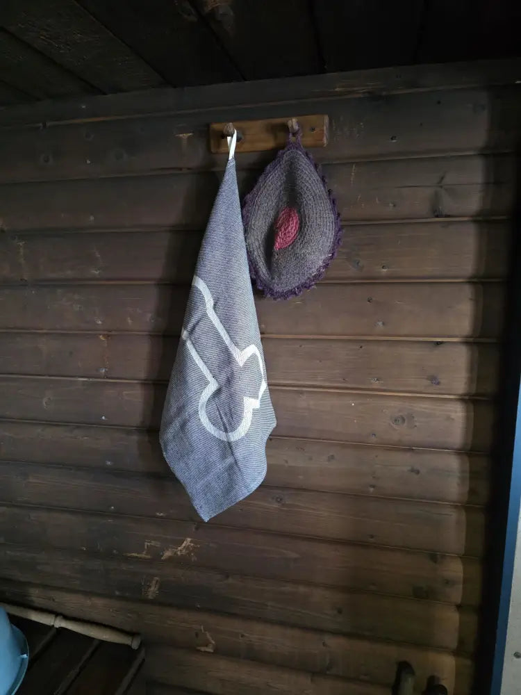 Pefletti Kalunalunen harmaa raidallinen pyyhe valkoisella brodeeratulla kuvioilla puukoukun päällä