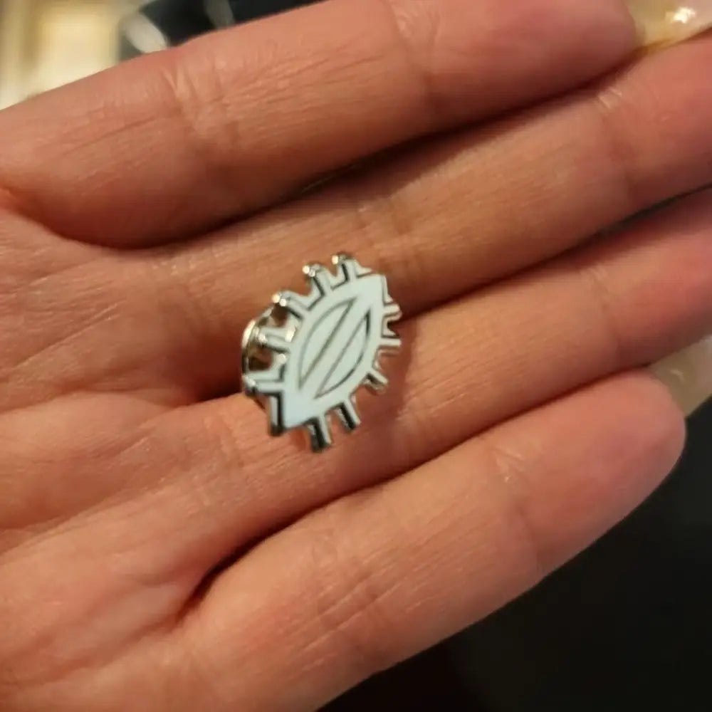 Silverinen enamel-pinssi, jossa pyörän ratasmainen muoto, ovaali keskus ja kolme pystysuoraa viivaa, pimppi pinssi