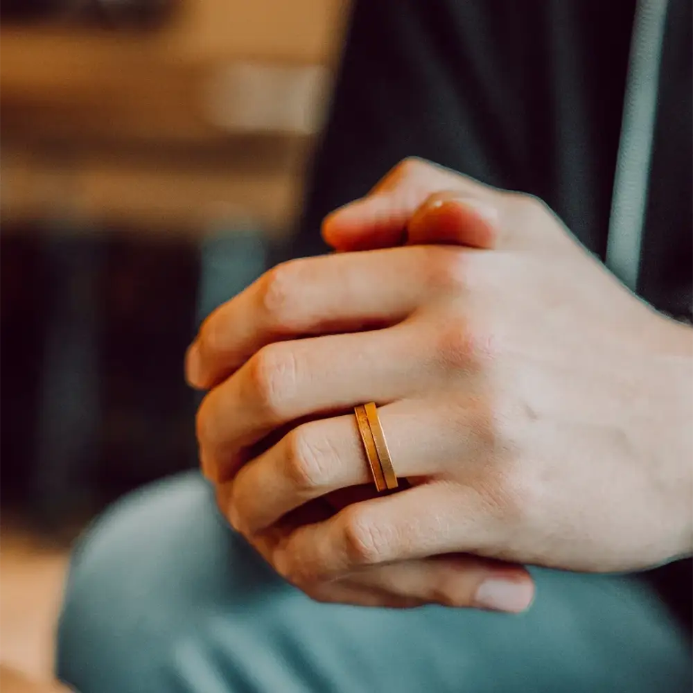 A sleek gold-toned puinen titaanisormus with a subtle textured finish worn on a finger