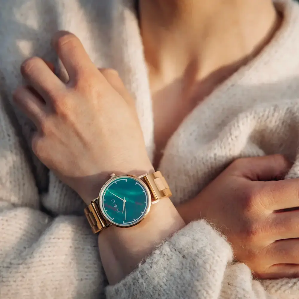 A delicate gold-toned wooden watch revontuli koivu with vibrant teal dial and minimalist design on a wrist