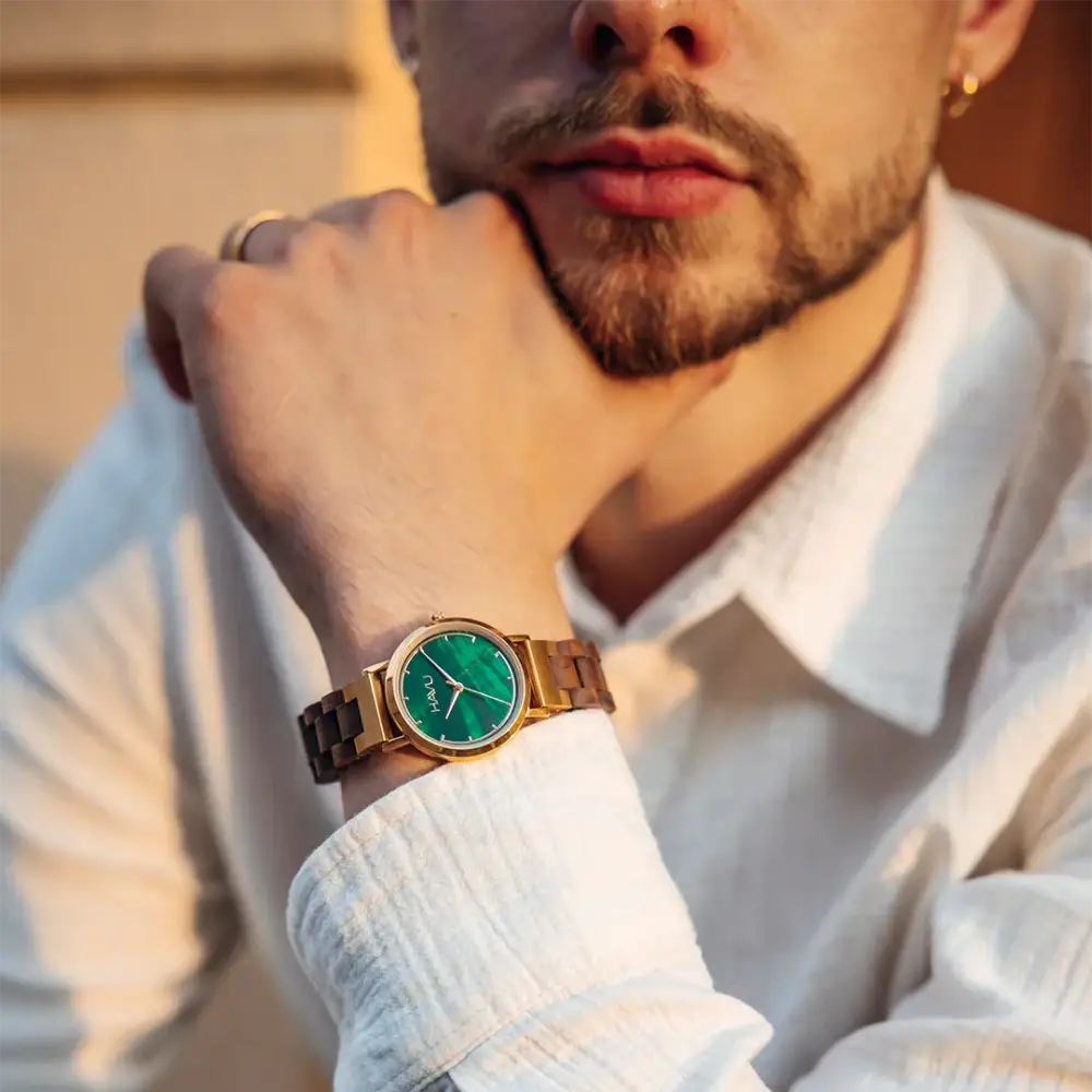 A sleek gold-toned wooden watch revontuli pähkinäpuu 32mm with a vibrant green dial worn on a mans wrist in ennakkotilaus