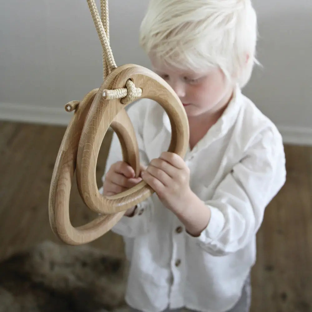 Natural-finish oak gymnastic rings with beige braided rope suspension for versatile fitness training