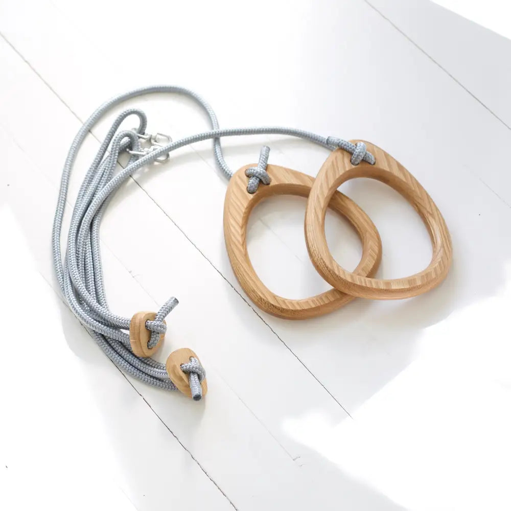Light-colored oak gymnastic rings with grey rope straps and matching knots for fitness training
