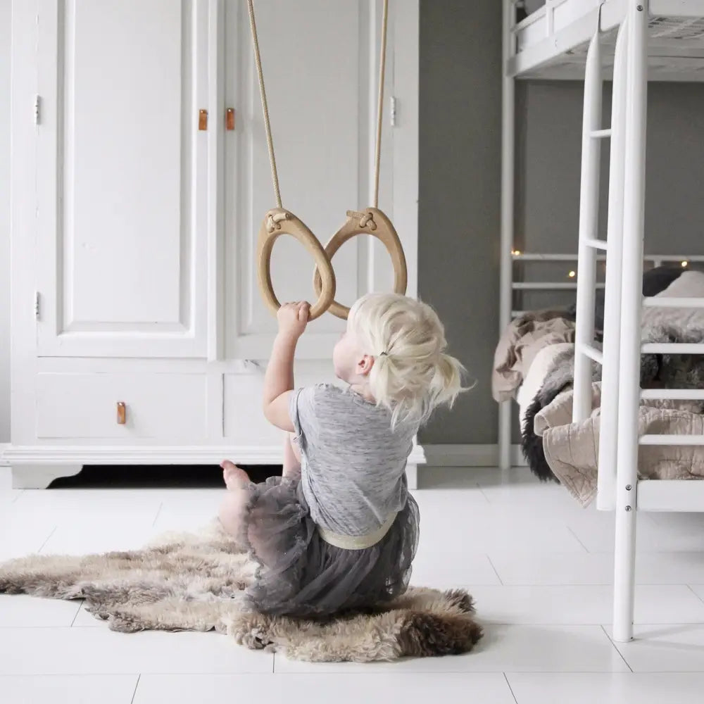 Light wood gymnastic rings suspended by rope in oak color with mint accents for fitness training