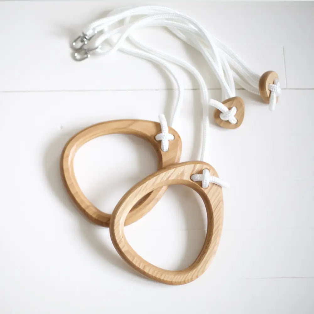 Light brown oak gymnastics rings with white rope straps and metal hooks for durable workout use
