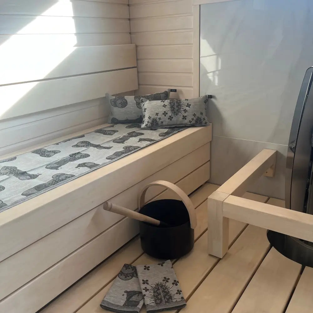 Light-colored wooden sauna bench with a saunatyyny Onnenkalu timber gray white towel and two matching pillows