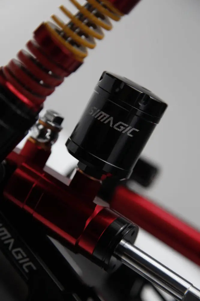 Black cylindrical brake fluid reservoir with silver magic lettering on red yellow motorcycle suspension in simagic p2000 3-pedal set
