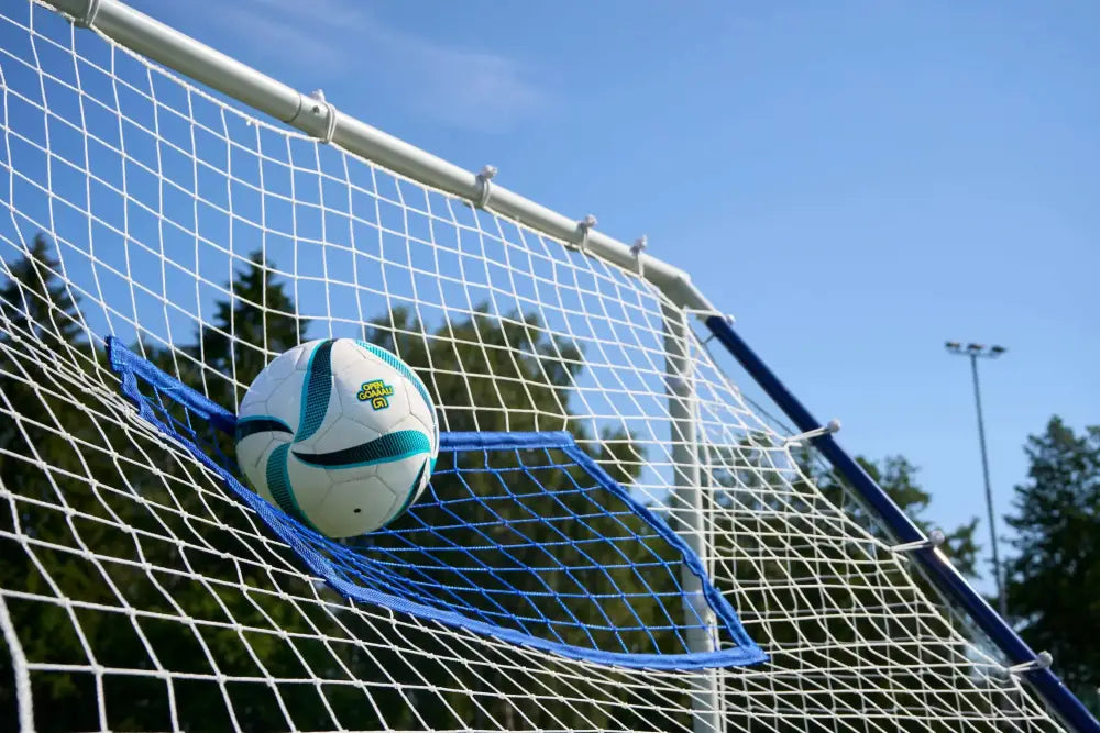 A white and teal textured soccer ball resting in the net of an outdoor triple function rebounder goal
