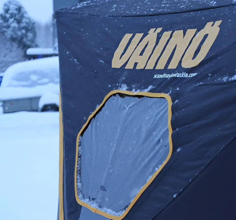 Dark blue uaino brand väinö bunker thermal extreme xxl pilkkiteltta with yellow-trimmed window and snow dusting