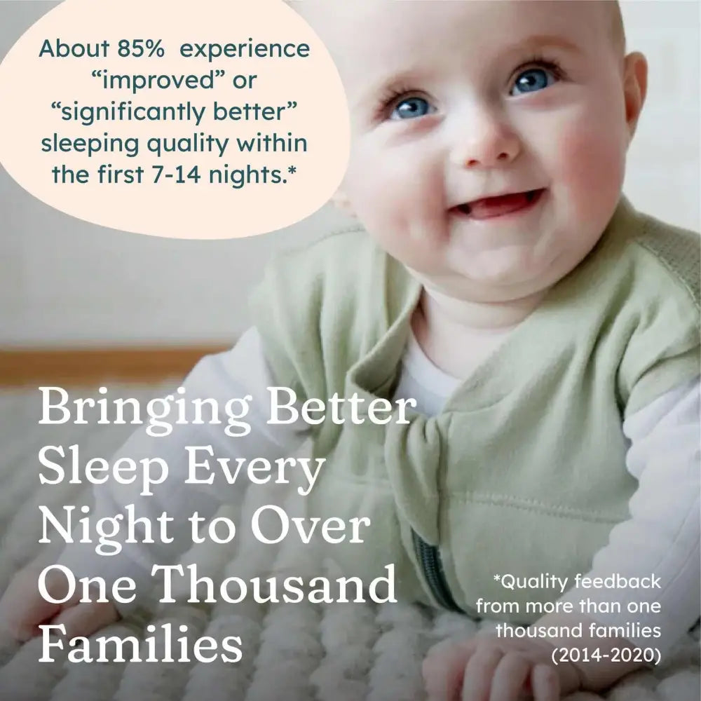 Hymyilevä vauva kirkkaansinisin silmin pehmeässä vaaleanvihreässä weighted swaddle i babydeepsleep® mini liivissä valkoisen paidan päällä